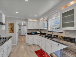 Kitchen featuring a sink, black electric stovetop, ornamental molding, white cabinetry, and decorative backsplash