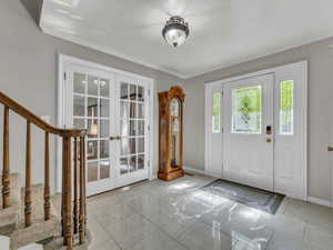 Foyer entrance featuring french doors, baseboards, crown molding, and stairway