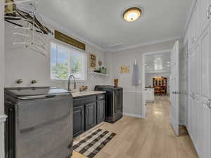 Laundry area with cabinet space, washer and clothes dryer, light wood-style floors, ornamental molding, and a chandelier