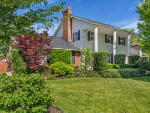 View of front of home with a chimney, a front yard, brick siding, and covered porch