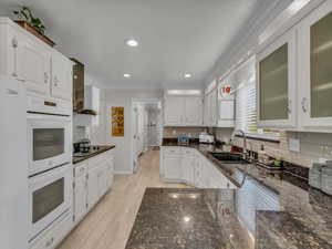 Kitchen with a sink, double oven, crown molding, white cabinets, and decorative backsplash
