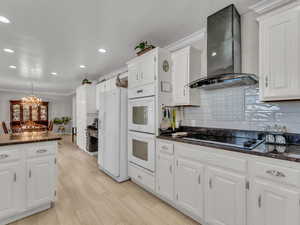 Kitchen featuring white appliances, island range hood, ornamental molding, white cabinetry, and backsplash