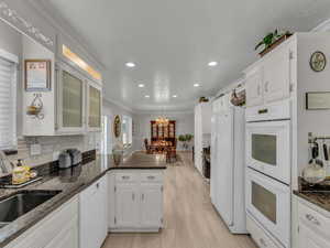 Kitchen with white appliances, a peninsula, white cabinetry, a sink, and recessed lighting