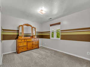 Bedroom with a textured ceiling, baseboards, and light carpet