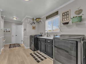 Laundry room featuring cabinet space, washer and clothes dryer, baseboards, light wood-type flooring, and ornamental molding
