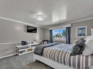 Carpeted bedroom featuring crown molding, a textured ceiling, baseboards, and a chandelier