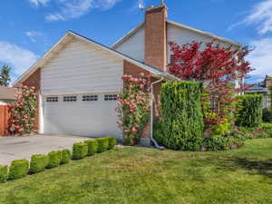 View of front of property featuring a chimney, concrete driveway, brick siding, a garage, and a front yard