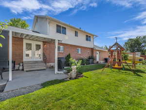 Rear view of house featuring a playground, a yard, a patio area, french doors, and brick siding