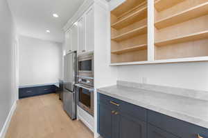 Kitchen featuring stainless steel appliances, open shelves, blue cabinetry, white cabinetry, and light wood finished floors