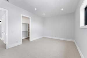 Unfurnished bedroom featuring light carpet, recessed lighting, a walk in closet, and baseboards