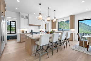 Kitchen featuring an island with sink, custom range hood, decorative backsplash, light wood-type flooring, and recessed lighting