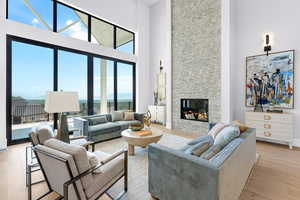 Living area with a towering ceiling, light wood-type flooring, a fireplace, baseboards, and a water view