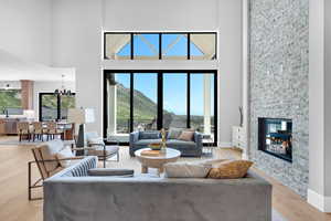 Living room featuring a high ceiling, light wood-style floors, a stone fireplace, baseboards, and a mountain view