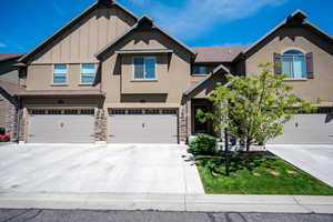 View of front facade featuring concrete driveway, stucco siding, a garage, board and batten siding, and stone siding