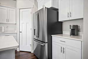 Kitchen featuring stainless steel refrigerator with ice dispenser, light countertops, white cabinets, and dark wood-style flooring