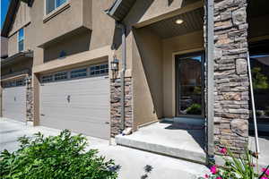 Entrance to property with stucco siding, stone siding, and an attached garage
