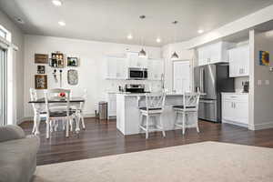 Kitchen featuring stainless steel appliances, a breakfast bar, white cabinetry, dark wood-type flooring, and recessed lighting