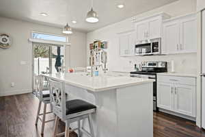 Kitchen with stainless steel appliances, dark wood-style flooring, a breakfast bar area, an island with sink, and baseboards