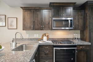 Kitchen with stainless steel microwave, stove, a sink, and dark brown cabinets