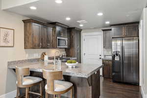 Kitchen with appliances with stainless steel finishes, dark brown cabinetry, a peninsula, dark wood finished floors, and a sink