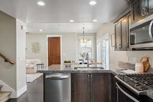 Kitchen with appliances with stainless steel finishes, a sink, dark brown cabinets, a peninsula, and light stone countertops