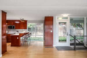 Kitchen featuring stainless steel microwave, light wood-style floors, a breakfast bar area, and dark brown cabinets