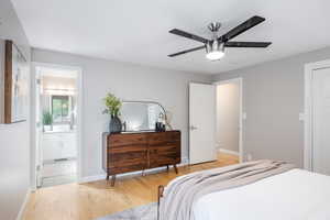 Bedroom with light wood-style flooring, baseboards, ensuite bathroom, and ceiling fan