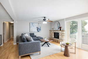 Living room featuring light wood finished floors, ceiling fan, a stone fireplace, and baseboards
