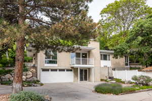 View of front of property with a balcony, driveway, brick siding, a garage, and central AC unit