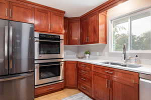 Kitchen featuring stainless steel appliances, a sink, light countertops, brown cabinets, and light wood-style flooring