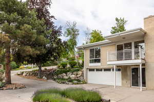 View of side of home with a balcony, driveway, a garage, and stairway