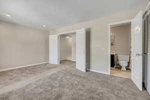 Unfurnished bedroom with light colored carpet, ensuite bath, recessed lighting, and baseboards