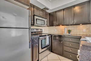 Kitchen with stainless steel appliances, light tile patterned floors, decorative backsplash, and dark brown cabinets