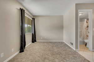 Unfurnished bedroom with light colored carpet, baseboards, and connected bathroom