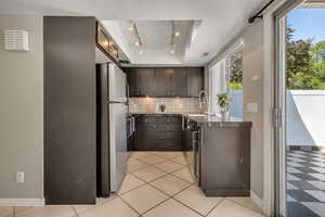 Kitchen featuring freestanding refrigerator, backsplash, rail lighting, a sink, and dark countertops