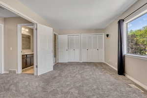Unfurnished bedroom featuring two closets, light carpet, ensuite bathroom, and baseboards