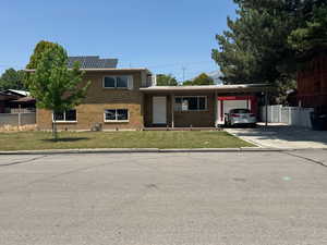 View of front of property featuring an attached garage, brick siding, concrete driveway, roof mounted solar panels, and a carport