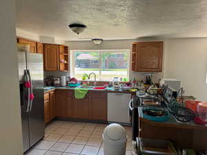 Kitchen featuring stainless steel fridge with ice dispenser, white dishwasher, open shelves, a sink, and brown cabinetry