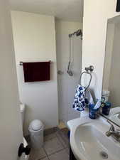 Full bathroom with toilet, tiled shower, a sink, tile patterned flooring, and a textured ceiling