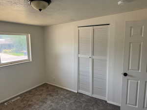 Unfurnished bedroom with a closet, a textured ceiling, dark carpet, and baseboards