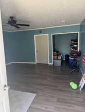Unfurnished room featuring ceiling fan, a textured ceiling, wood finished floors, ornamental molding, and a smoke detector
