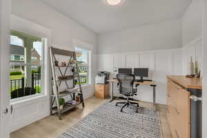 Office with a decorative wall, light wood-style flooring, and wainscoting