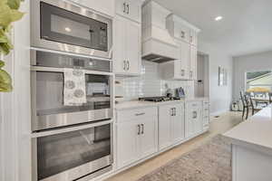 Kitchen with custom range hood, stainless steel appliances, decorative backsplash, light wood-type flooring, and recessed lighting