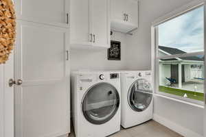Laundry area with separate washer and dryer, cabinet space, and light tile patterned floors