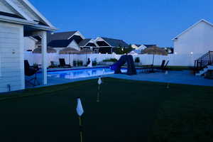 View of pool with a putting area, a water slide, a fenced backyard, and a patio