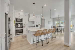 Kitchen featuring custom range hood, appliances with stainless steel finishes, light countertops, a kitchen breakfast bar, and decorative backsplash