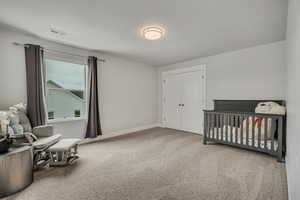 Carpeted bedroom featuring a closet, baseboards, and a nursery area