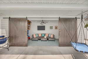 Living room with a barn door, a ceiling fan, and beam ceiling