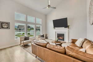Living area with high vaulted ceiling, a ceiling fan, a glass covered fireplace, light wood-style floors, and baseboards