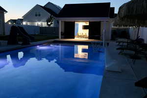 Pool at dusk with a water slide, a fenced backyard, and a patio